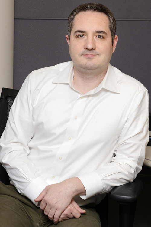 A young man in a dress shirt sits in an office cubicle