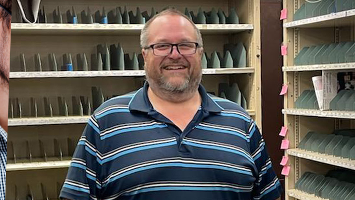 A man stands in a Post Office workroom, smiling