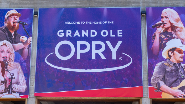 An exterior shot of the Grand Ole Opry with a banner above the front doors displaying images of country music stars such as Dolly Parton