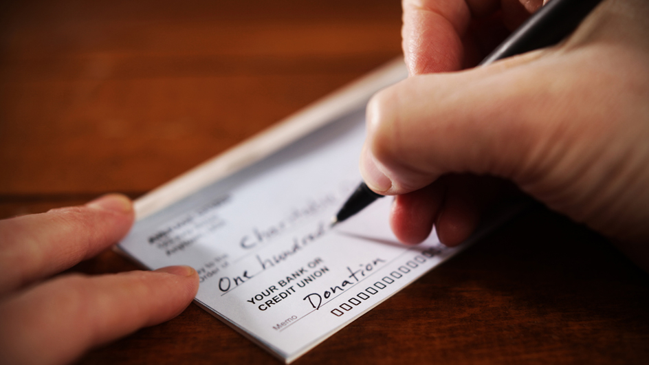 A person’s hands are shown writing a check for a charitable donation