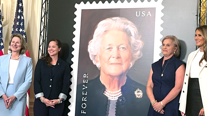 Women stand next to a large poster of a Barbara Bush stamp image