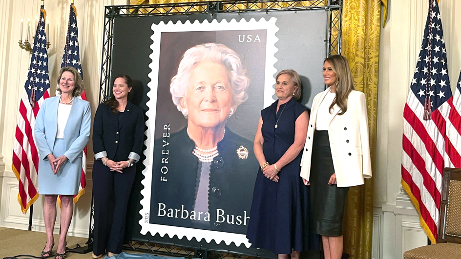 Women stand next to a large poster of a Barbara Bush stamp image