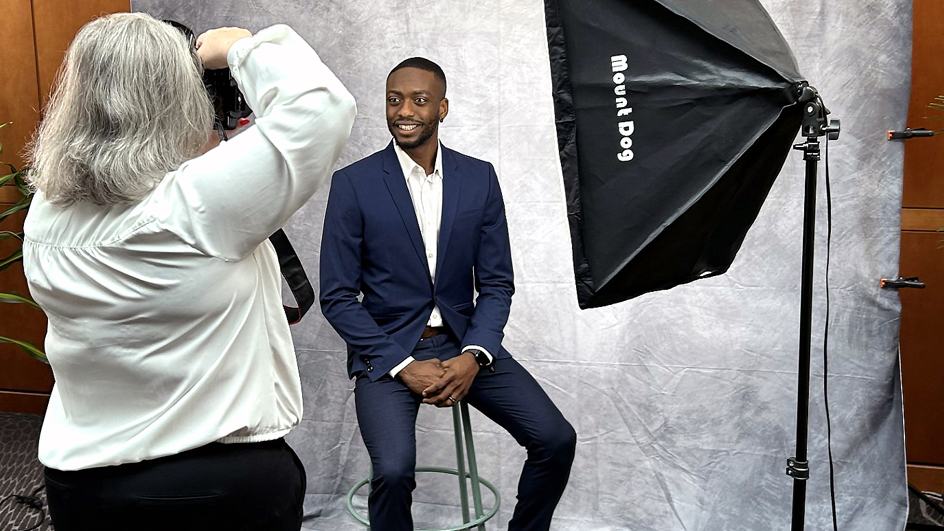 A man in a sport coat smiles brightly as a photographer snaps his picture