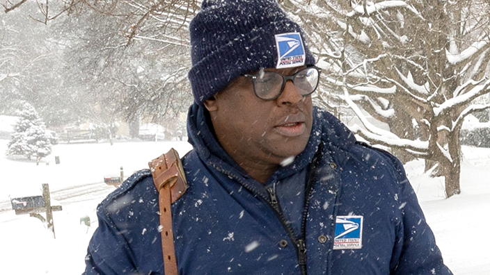 A letter carrier trudges through a snowy sidewalk