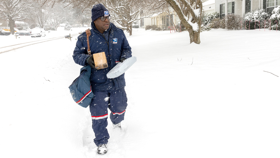 A letter carrier trudges through a snowy sidewalk