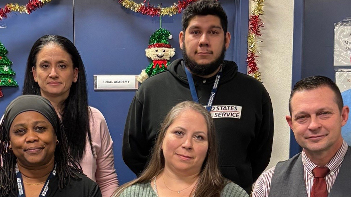 Eight people sit in two rows of chairs in a Post Office workroom