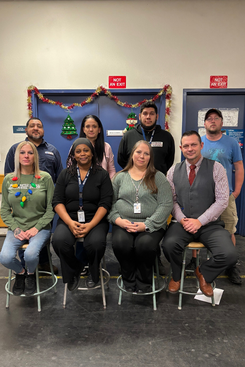 Eight people sit in two rows of chairs in a Post Office workroom