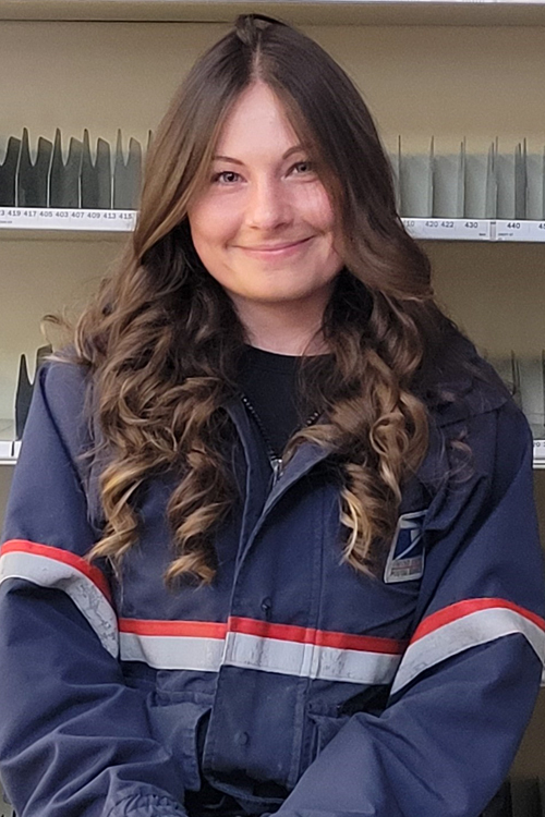 A woman wearing a postal uniform stands in a Post Office workroom