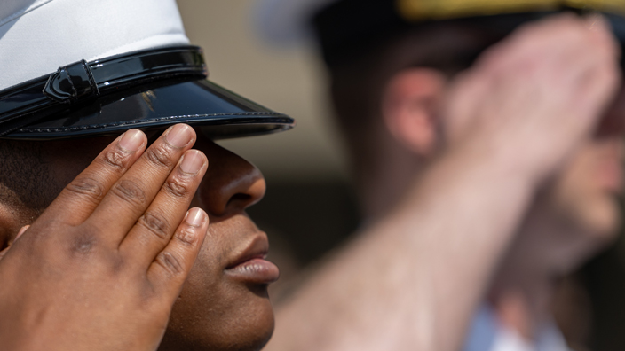 A tight shot of two men in naval uniforms saluting