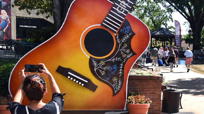 A woman uses her smartphone to take a picture of a guitar statue outside the Grand Ole Opry house