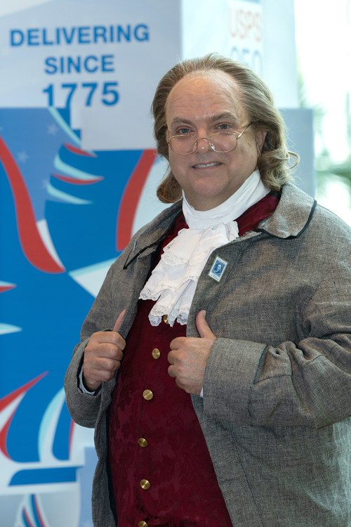 A man dressed as Ben Franklin stands on a convention room floor.