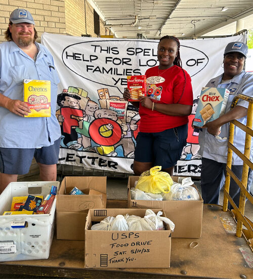 Three people stand on a Post Office loading dock near a large box of canned and boxed food