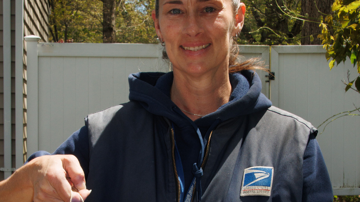 A woman in a postal uniform holds up a plastic bag filled with food
