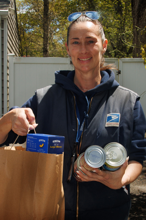 A woman in a postal uniform holds up a plastic bag filled with food