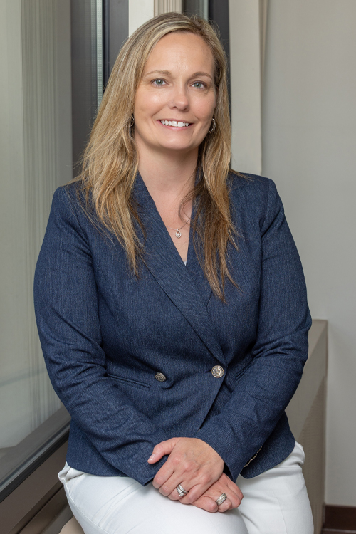 A woman sits at a desk in an office, smiling