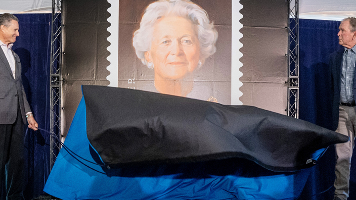 People stand on a stage and remove a curtain covering a poster bearing a Barbara Bush stamp image