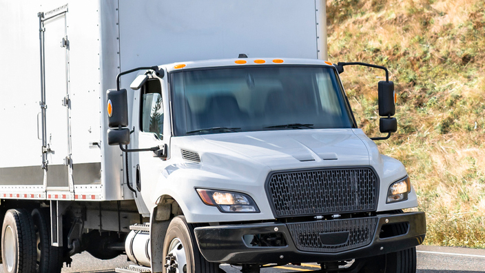 A white box truck moves down a roadway