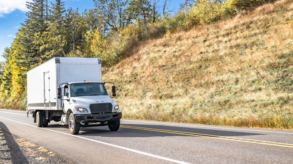 A white box truck moves down a roadway
