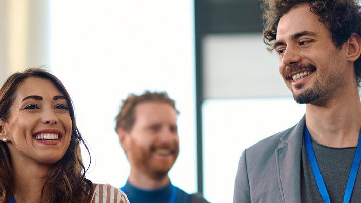 People wearing badges around their necks walk and talk in a conference setting