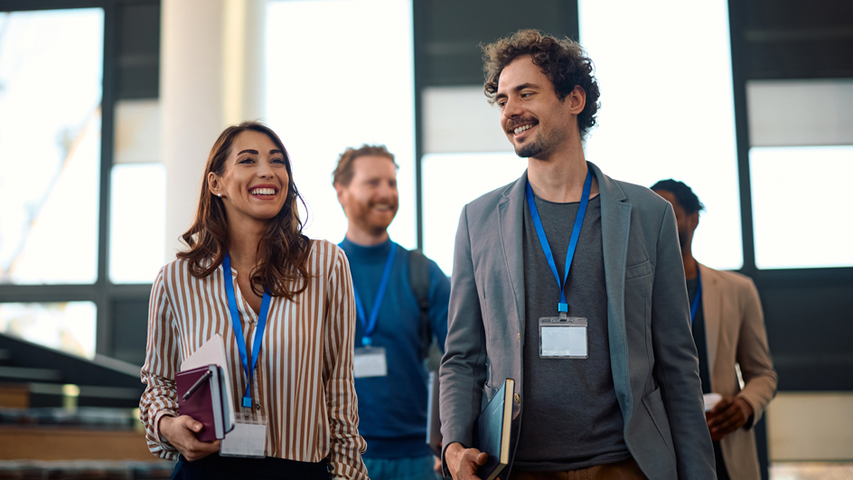 People wearing badges around their necks walk and talk in a conference setting