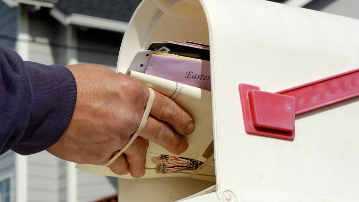 A hand places a letter inside a mailbox