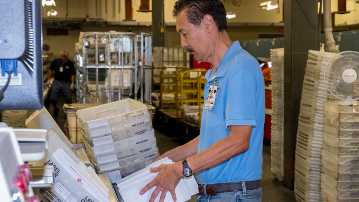A man operates mail processing equipment inside a USPS plan