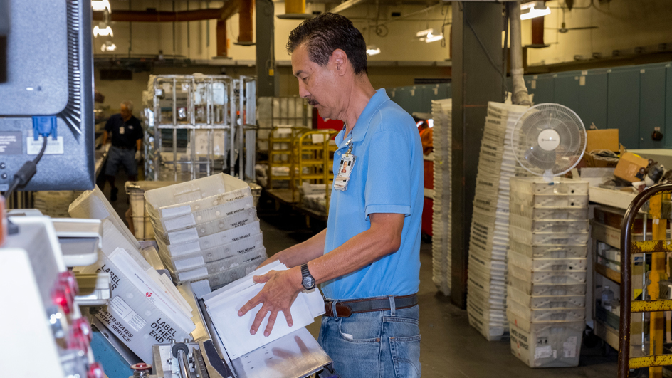 A man operates mail processing equipment inside a USPS plan