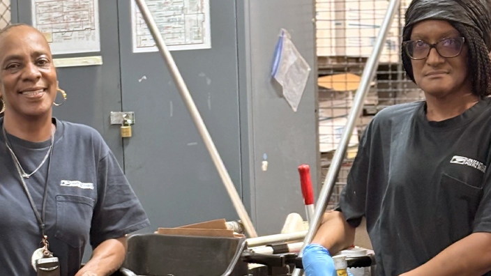 Two women smile and stand among cleaning carts and equipment