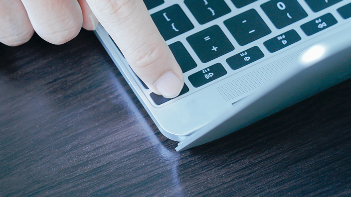 A man’s finger presses the start button on a laptop keyboard