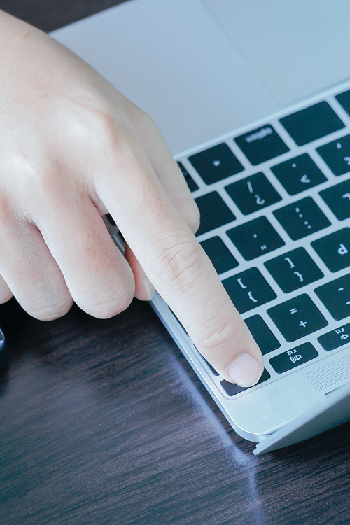 A man’s finger presses the start button on a laptop keyboard