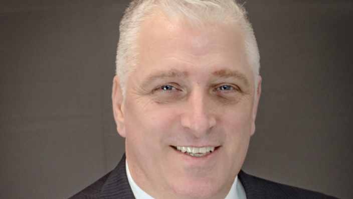 A studio portrait of a main wearing a jacket and tie.