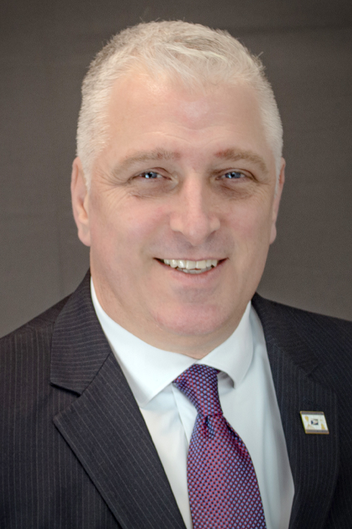 A studio portrait of a main wearing a jacket and tie.