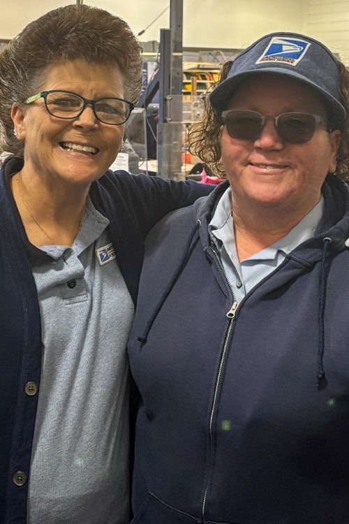 Two women wearing postal uniforms stand next to each other