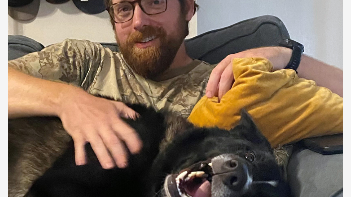 A man sits on a sofa with a dog on his lap
