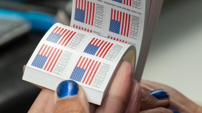 A woman’s hands hold several booklets of stamps bearing an image of the U.S. Flag.