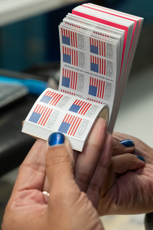 A woman’s hands hold several booklets of stamps bearing an image of the U.S. Flag.