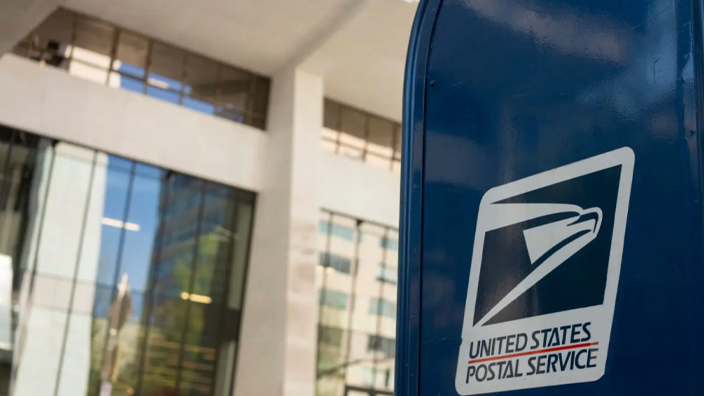 A blue USPS collection box on a city sidewalk
