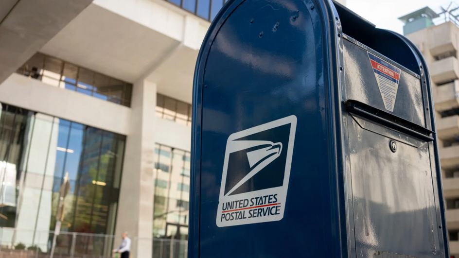 A blue USPS collection box on a city sidewalk
