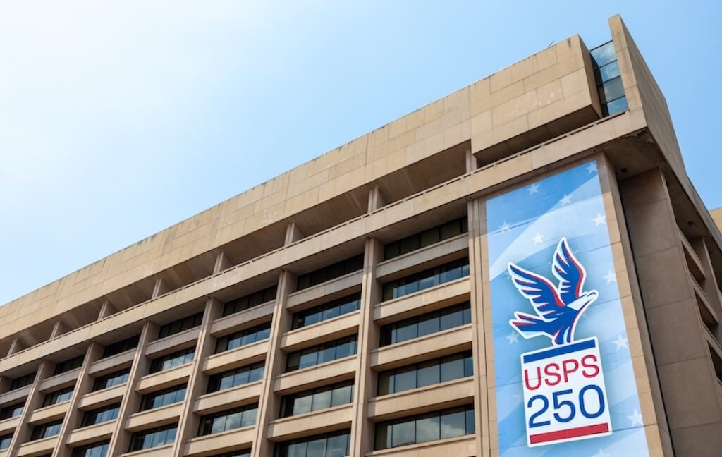 A large banner hanging on the side of an office building. The banner shows an illustration of an eagle about to take wing and the words “USPS 250.”