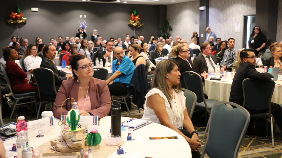 People sit at tables in a hotel ballroom and listen to an unseen speaker