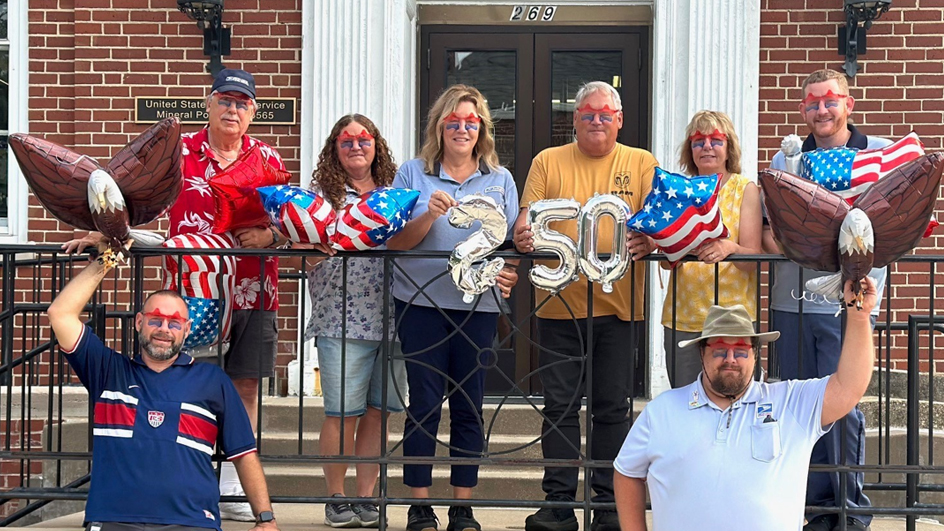 People wearing patriotic colors stand outside a brick Post Office