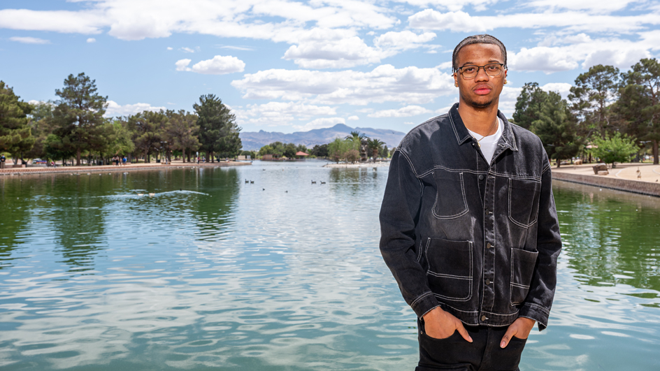A young man stands near a lake