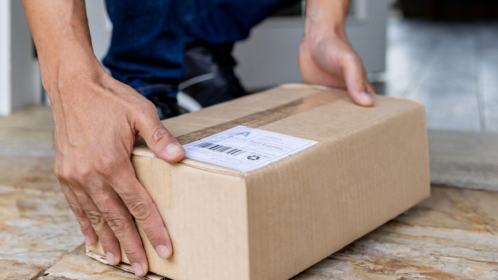 A man leans down to retrieve a package from a front porch