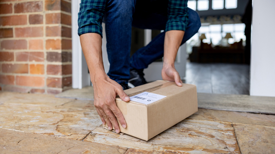 A man leans down to retrieve a package from a front porch