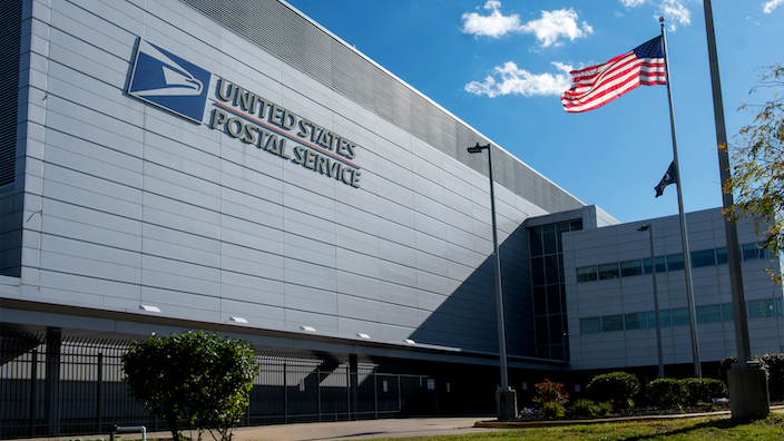 The exterior of a large USPS building with an American flag flying outside