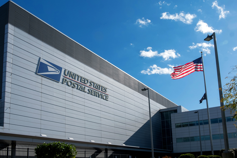 The exterior of a large USPS building with an American flag flying outside