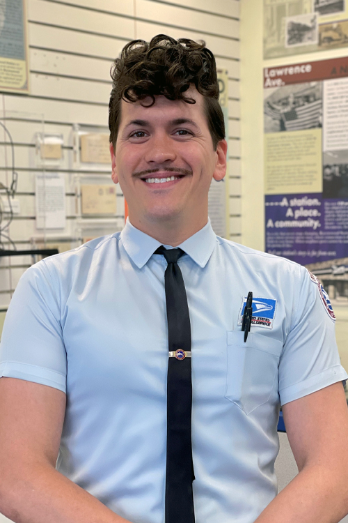 A sharply dressed postal worker stands in a Post Office lobby