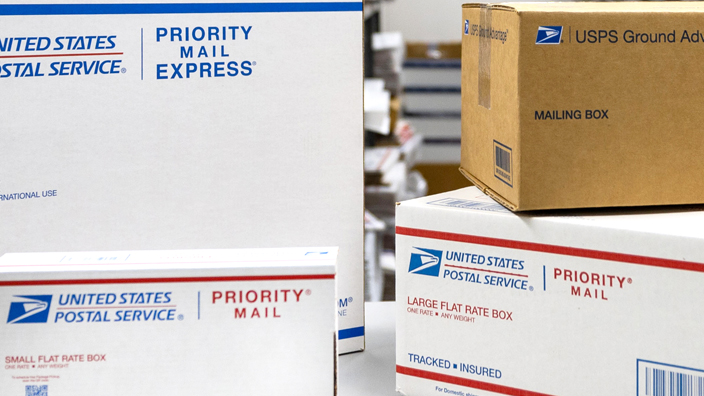 An array of USPS-branded shipping boxes displayed on a table in a Post Office workroom