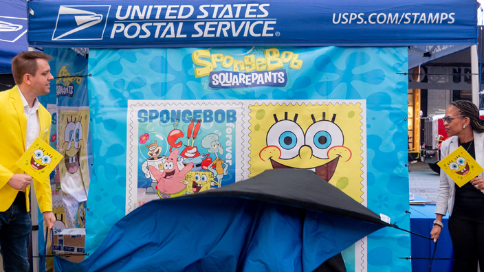 A man and a woman pull down a curtain covering a poster displaying cartoon character stamp images