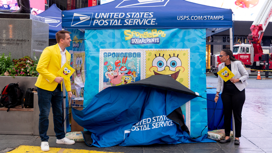 A man and a woman pull down a curtain covering a poster displaying cartoon character stamp images